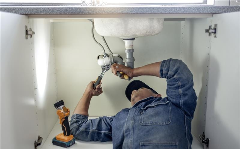 Plumber repairing pipes beneath a bathroom sink in Winder