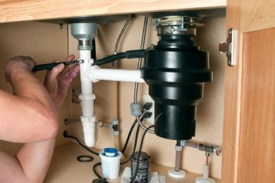 Plumber repairing a garbage disposal beneath a kitchen sink in Winder