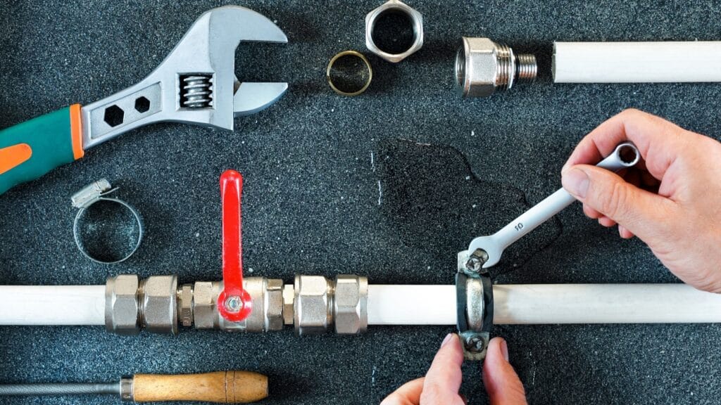 Plumber repairing a pipe valve with an adjustable wrench in Winder