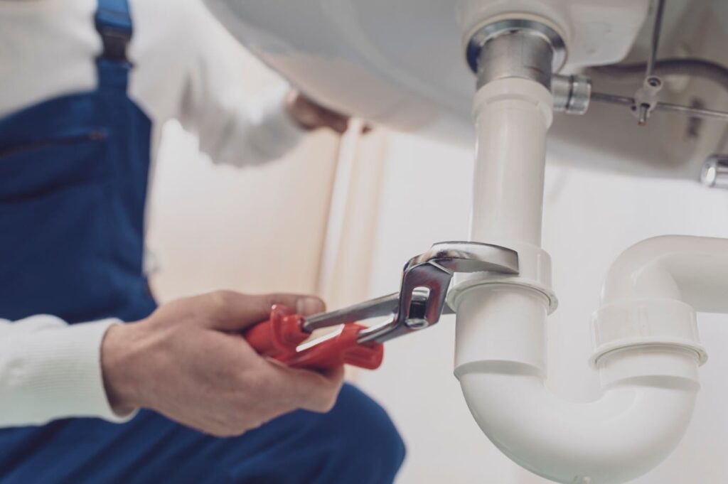 Plumber repairing a white drain pipe beneath a sink in Winder