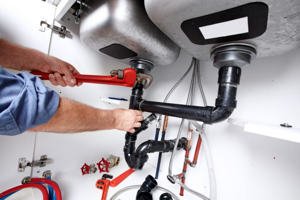 Plumber repairing drain pipes beneath a kitchen sink in Winder